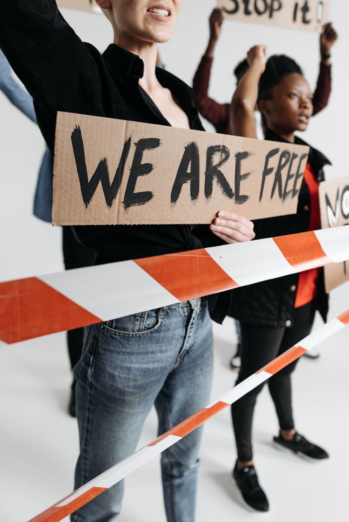 A group of diverse individuals protesting for freedom holding signs behind caution tape.